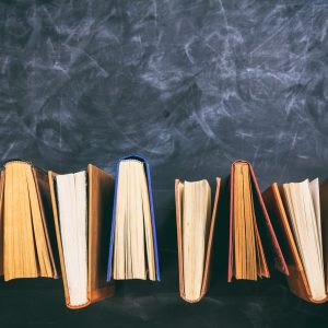 Vintage books standing on blackboard background - top view